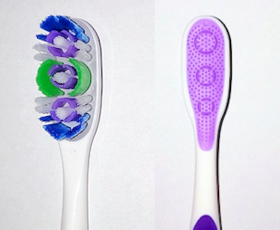 A sample toothbrush with thermoplastic elastic parts between the bristles and on the back.