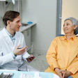 A dentist talks with an older woman, who is sitting in a dental chair.