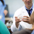 An orthodontist demonstrates braces to a patient using an acrylic model of the teeth.