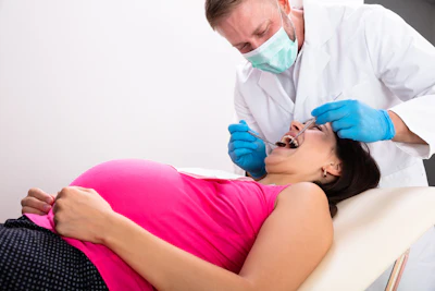 A dentist wearing a mask uses tools to inspect a pregnant women's teeth.
