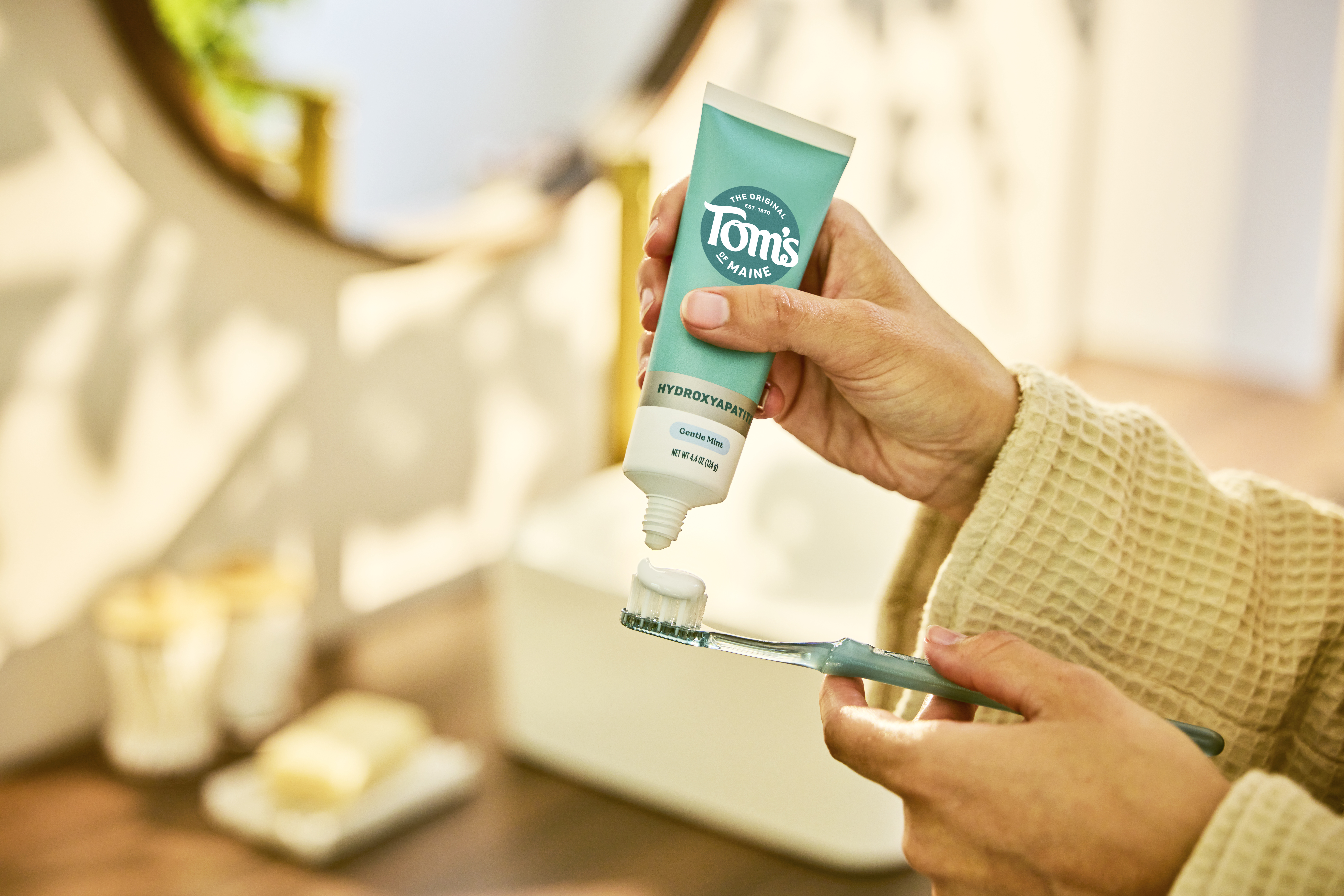 Close-up of a person applying Tom's of Maine toothpaste to a toothbrush.