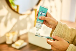 Close-up of a person applying Tom's of Maine toothpaste to a toothbrush.