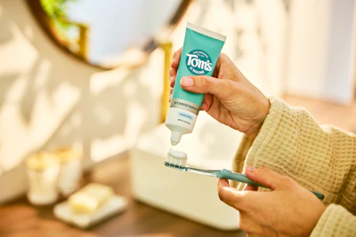 Close-up of a person applying Tom's of Maine toothpaste to a toothbrush.