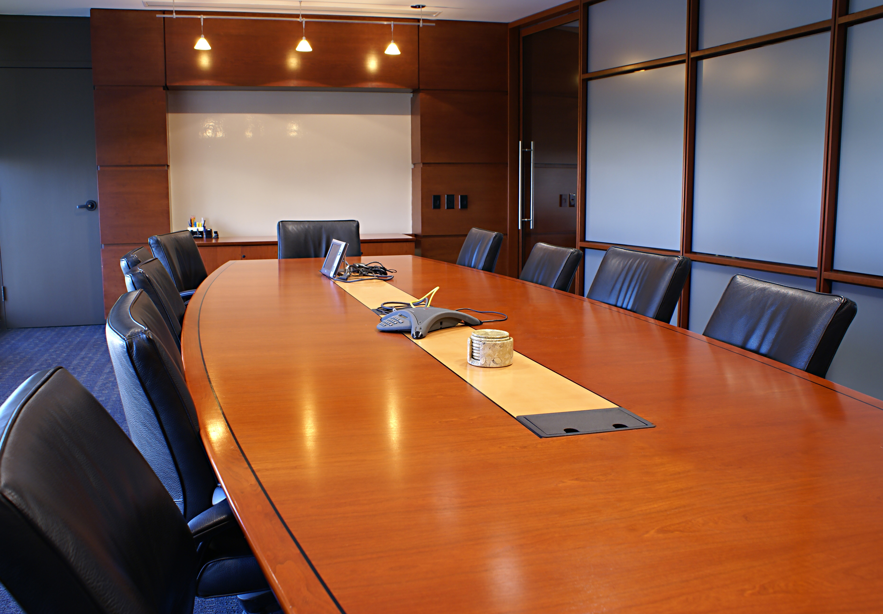 Modern conference room with a cherry wood table, leather chairs, a white board, and large windows.