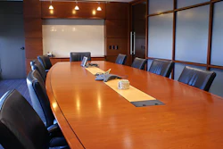 Modern conference room with a cherry wood table, leather chairs, a white board, and large windows.