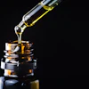 Golden liquid is dispersed from a dropper into an amber glass bottle.