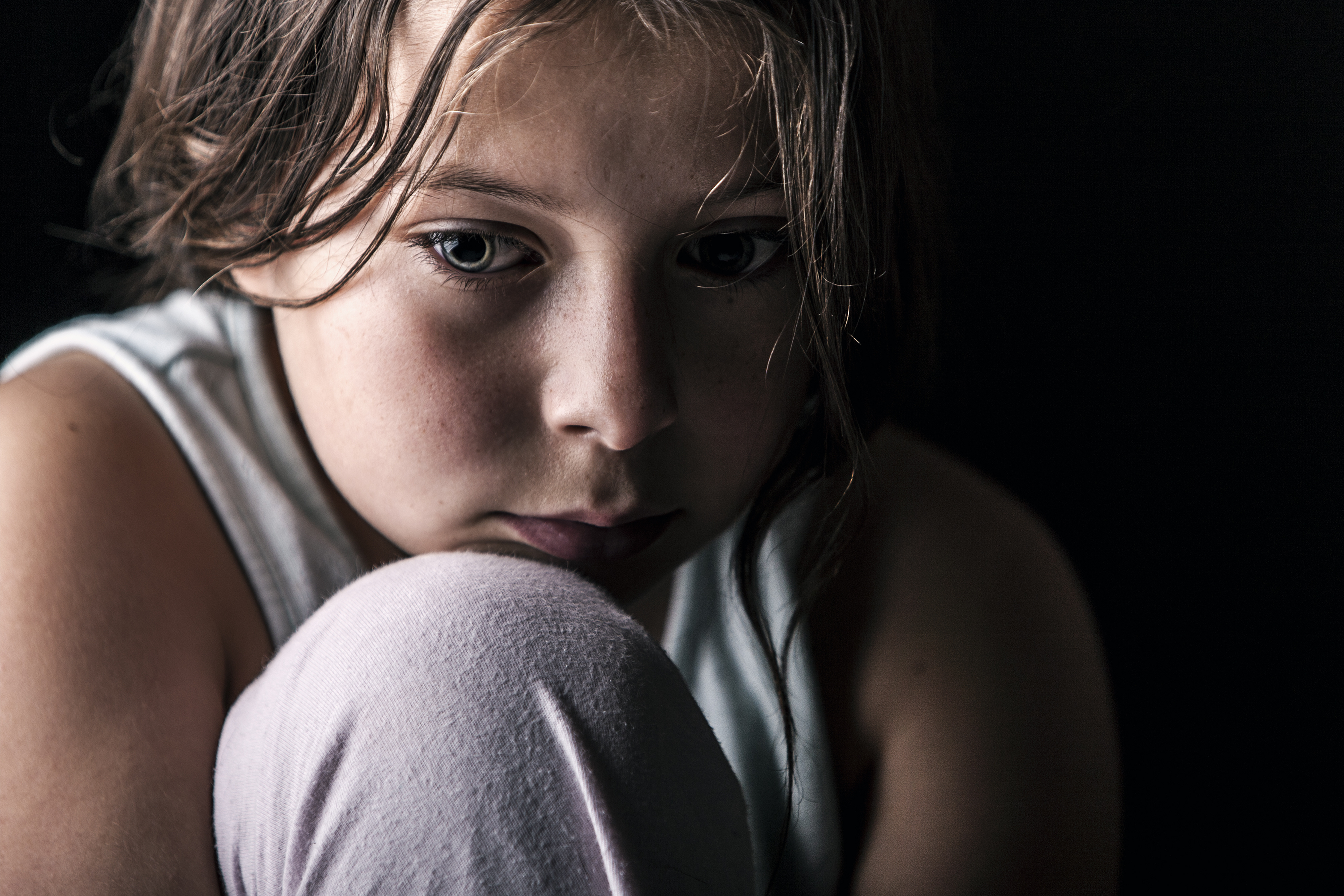 Close-up of a young, pensive girl with her chin resting on her knee.