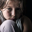 Close-up of a young, pensive girl with her chin resting on her knee.