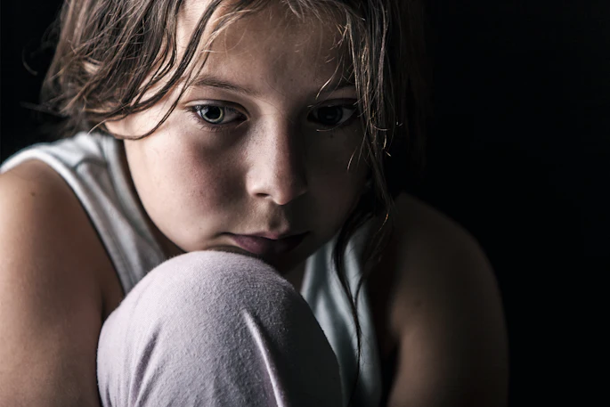 Close-up of a young, pensive girl with her chin resting on her knee.