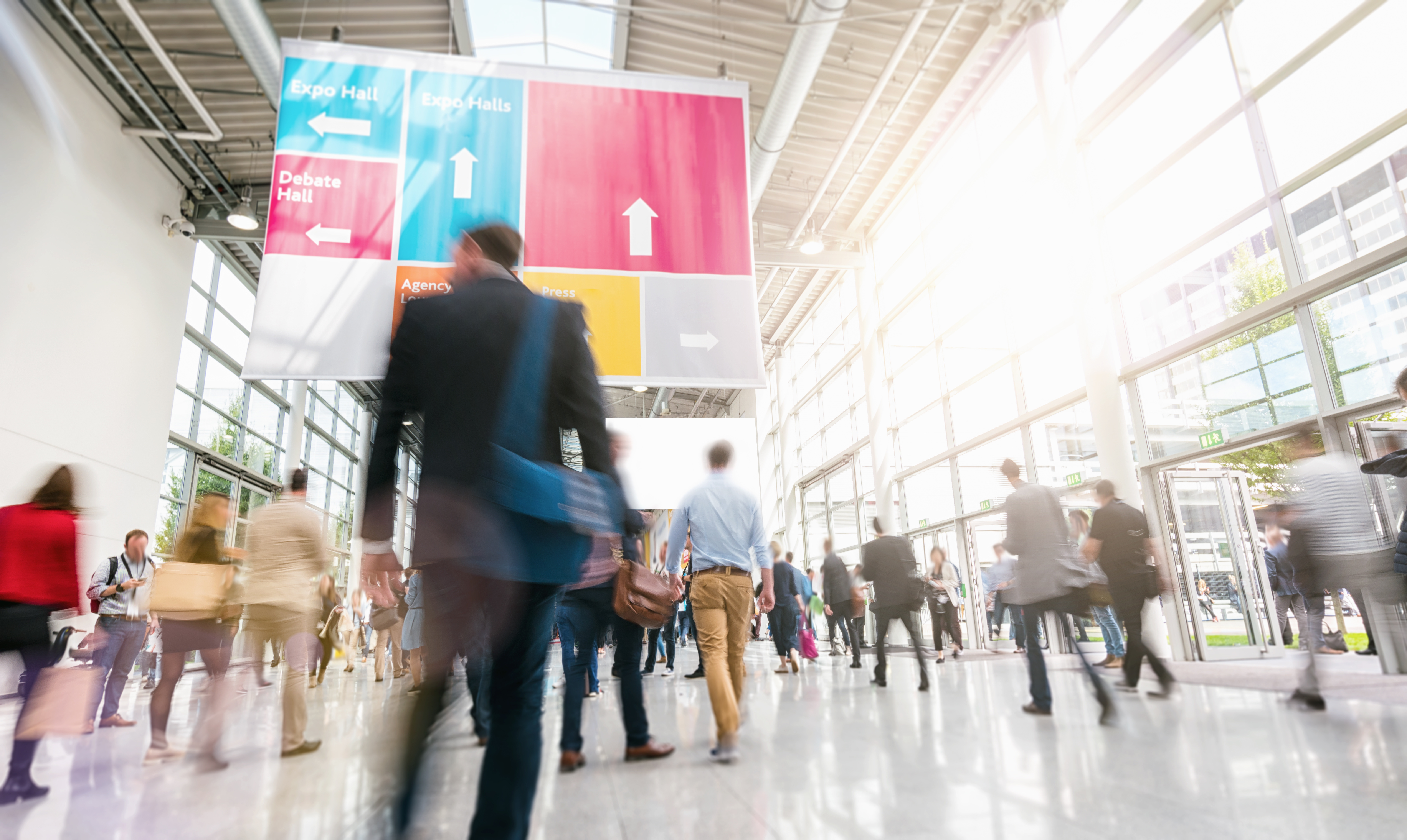 Blurred image of attendees in a sunlight convention center lobby.