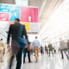 Blurred image of attendees in a sunlight convention center lobby.