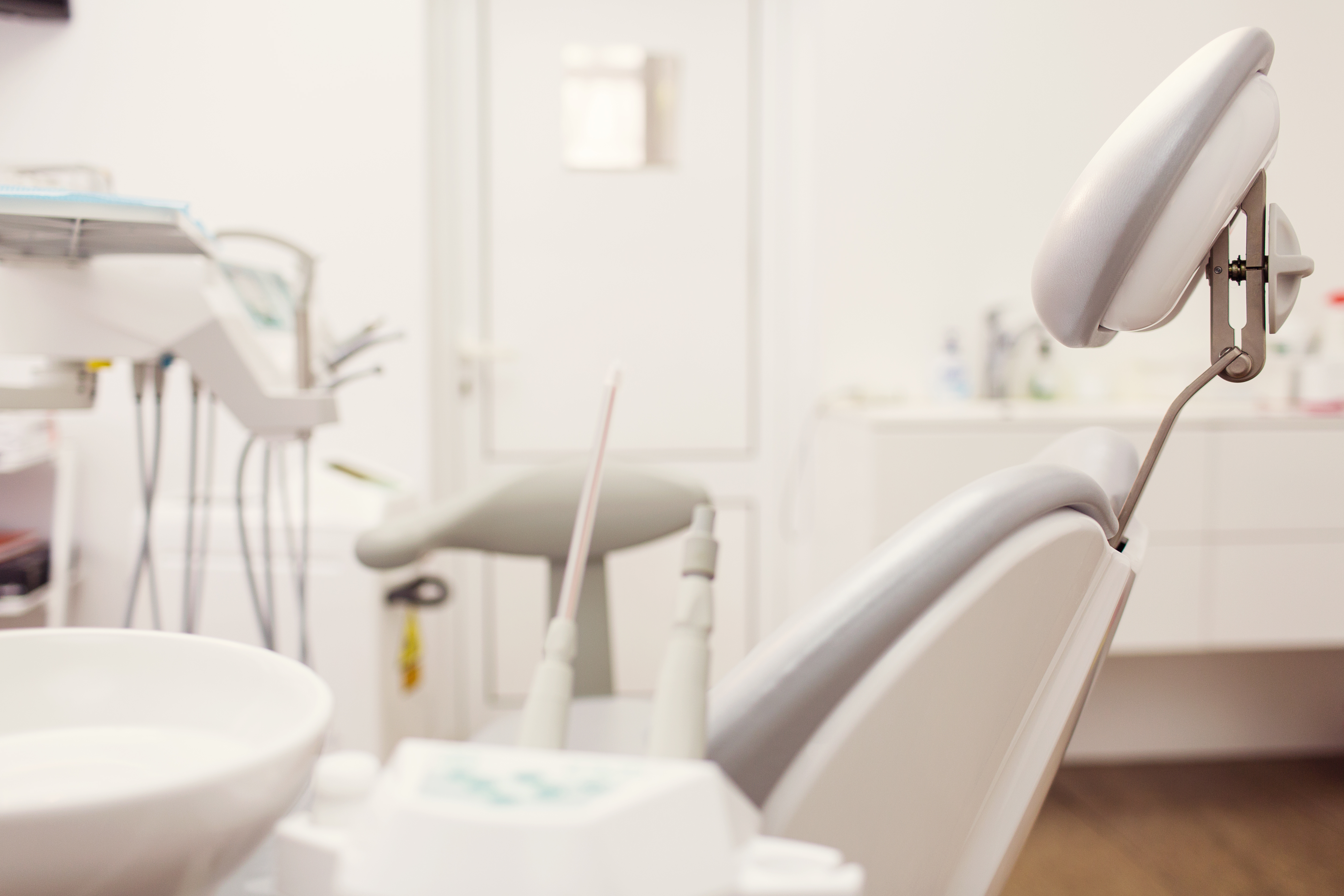 Modern, white dental office chair with a blurred white dental operatory in the background.