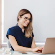 A woman dentist smiles as she looks at her laptop computer.