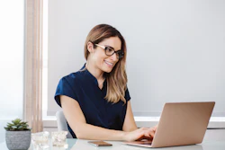 A woman dentist smiles as she looks at her laptop computer.