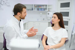 A male dentist talks to a young woman sitting in a dental chair.