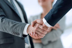 Two male business professionals wearing suits shake hands.