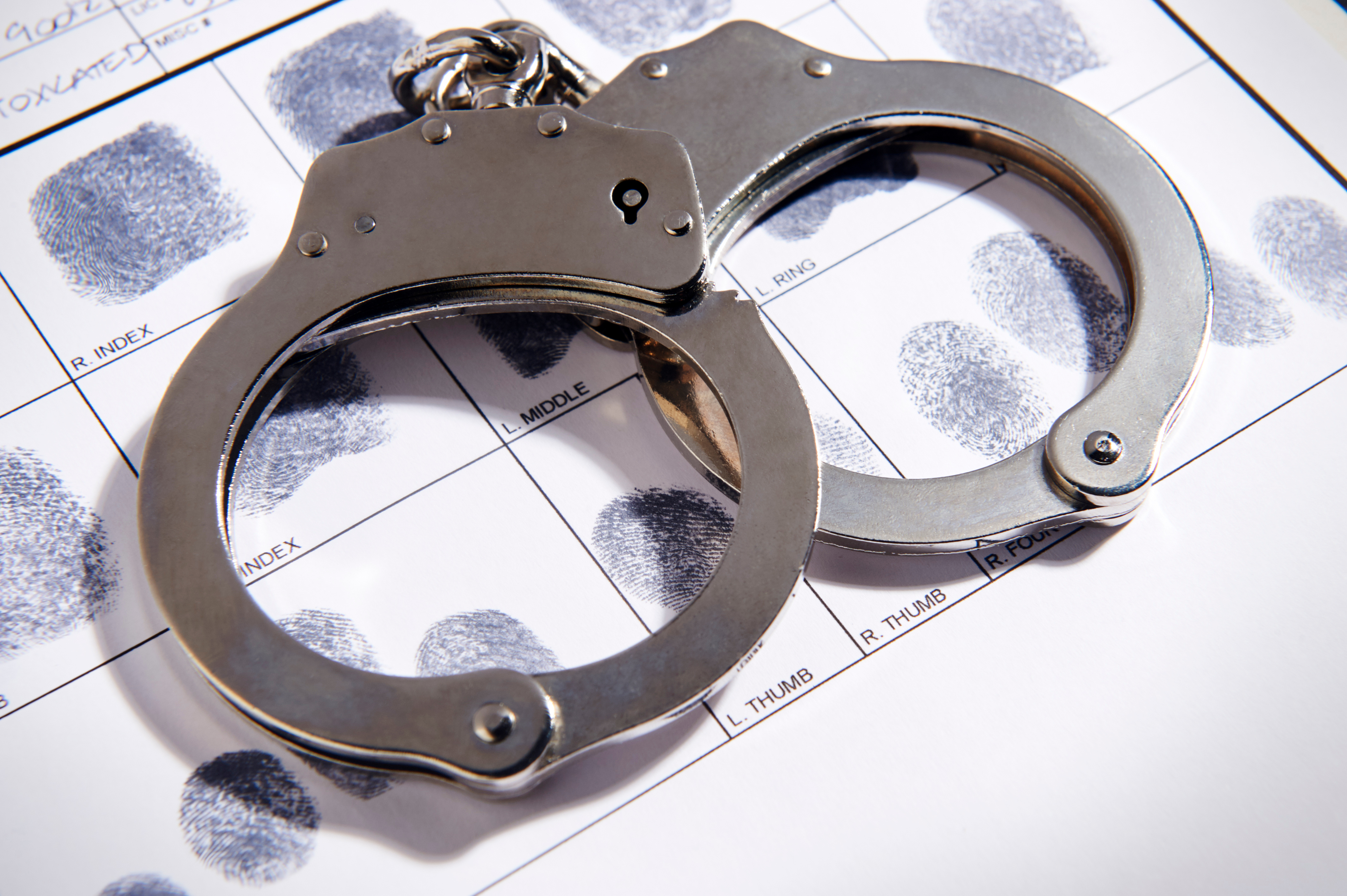 Metal handcuffs rest on top of a fingerprint identification card with inked fingerprints.