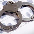 Metal handcuffs rest on top of a fingerprint identification card with inked fingerprints.