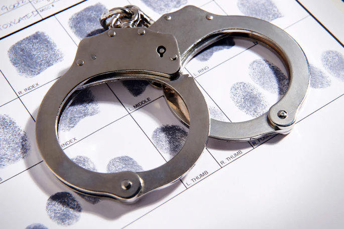 Metal handcuffs rest on top of a fingerprint identification card with inked fingerprints.