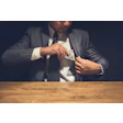 A businessman places a stack of $100 bills into his suit vest pocket.
