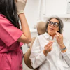 An older woman sits in a dental operatory chair and explains something to a woman dentist.