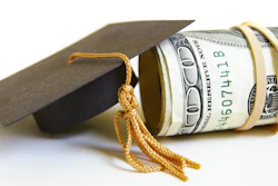 A graduation cap is positioned next to a roll of $100 bills.