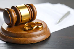 Two wedding rings rest with a wood gavel on a wood sound block symbolizing divorce proceedings.