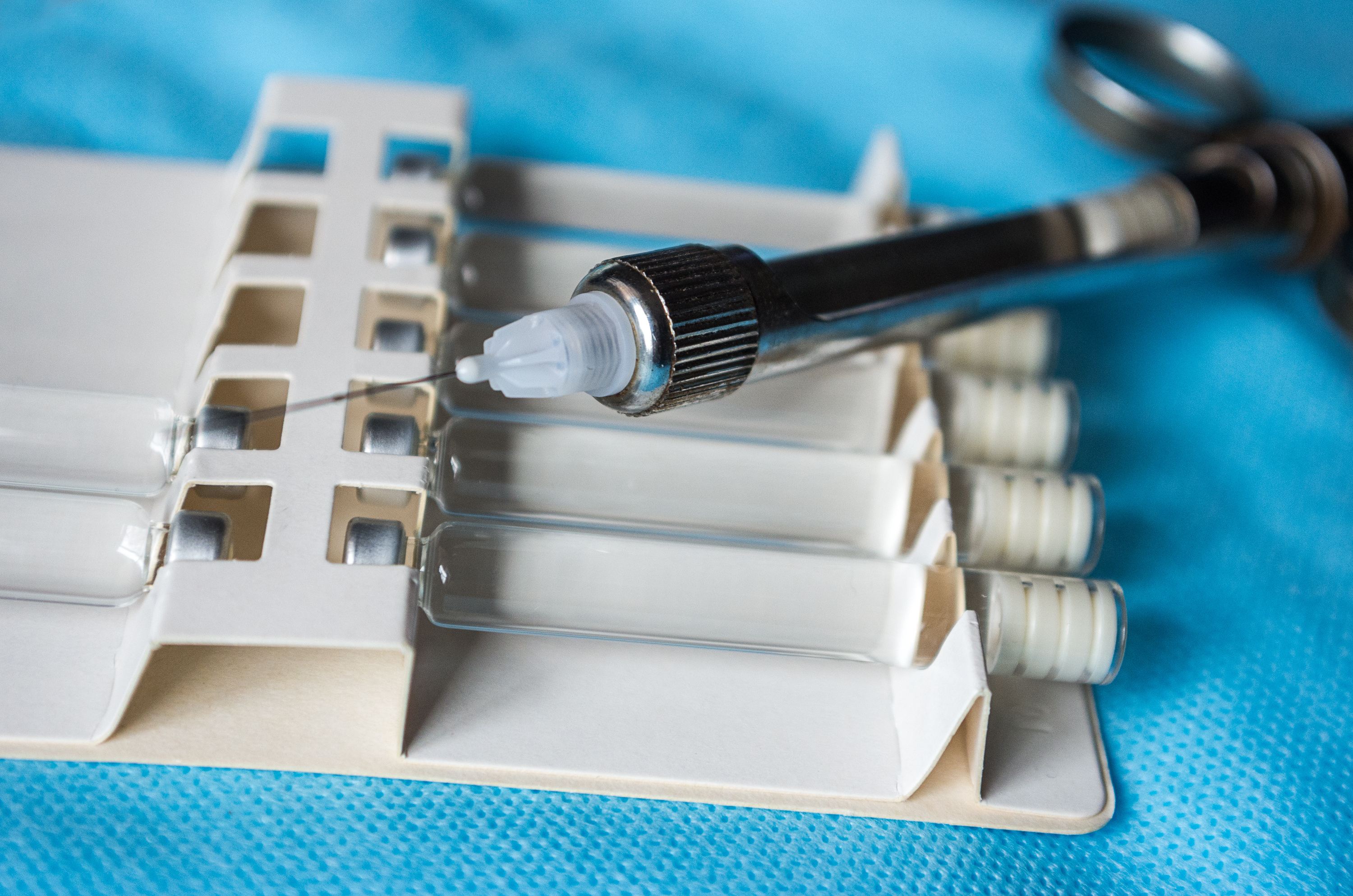 A dental syringe rests on top of vials of clear liquid.
