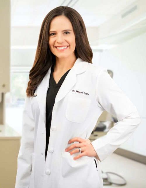 Female doctor in white lab coat smiling at camera in clinical office setting