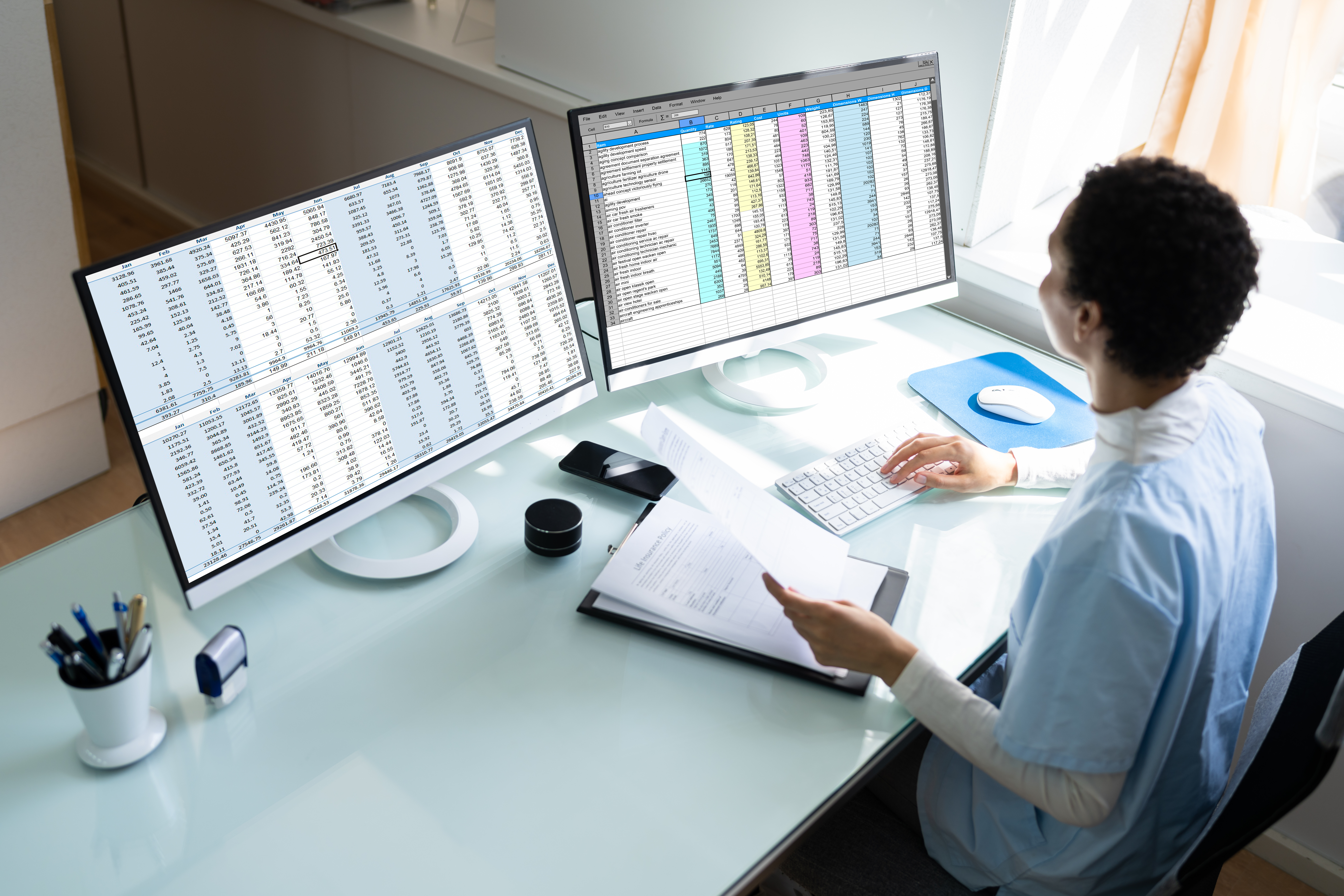 A woman medical insurance biller looks at a computer monitor. She is holding a paper in her left hand.