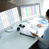 A woman medical insurance biller looks at a computer monitor. She is holding a paper in her left hand.