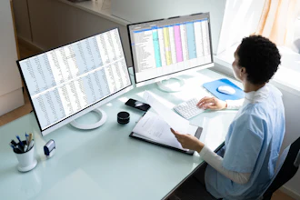 A woman medical insurance biller looks at a computer monitor. She is holding a paper in her left hand.