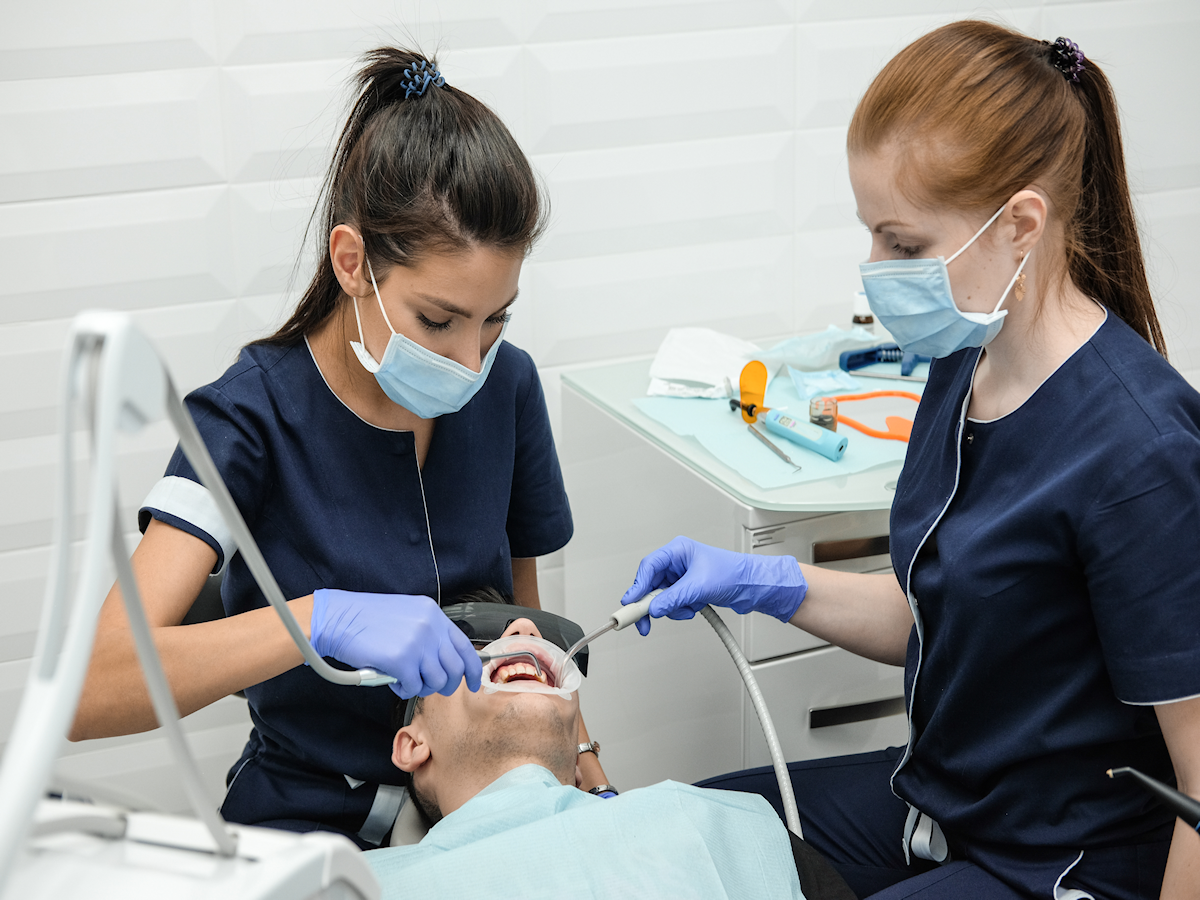 A dental assistant assists a woman dentist in suctioning a patient's mouth.