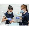 A dental assistant assists a woman dentist in suctioning a patient's mouth.