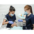 A dental assistant assists a woman dentist in suctioning a patient's mouth.