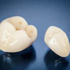 Two ceramic dental crowns lie on a glossy black surface.