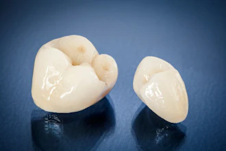 Two ceramic dental crowns lie on a glossy black surface.