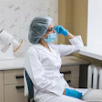 A woman healthcare worker wearing PPE looks out a window.