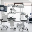 Modern dental operatory with treatment chair, overhead surgical microscope, digital imaging monitor, and professional equipment in a bright clinical setting.