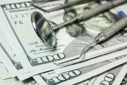 Dental tools lie on top of several $100 bills.
