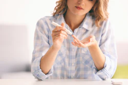 A young woman holds a diabetes lancet to a finger. She is going to perform a blood glucose test.