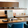 Modern executive office with a wooden desk, white chair, computer monitor, and wall-mounted storage cabinets.
