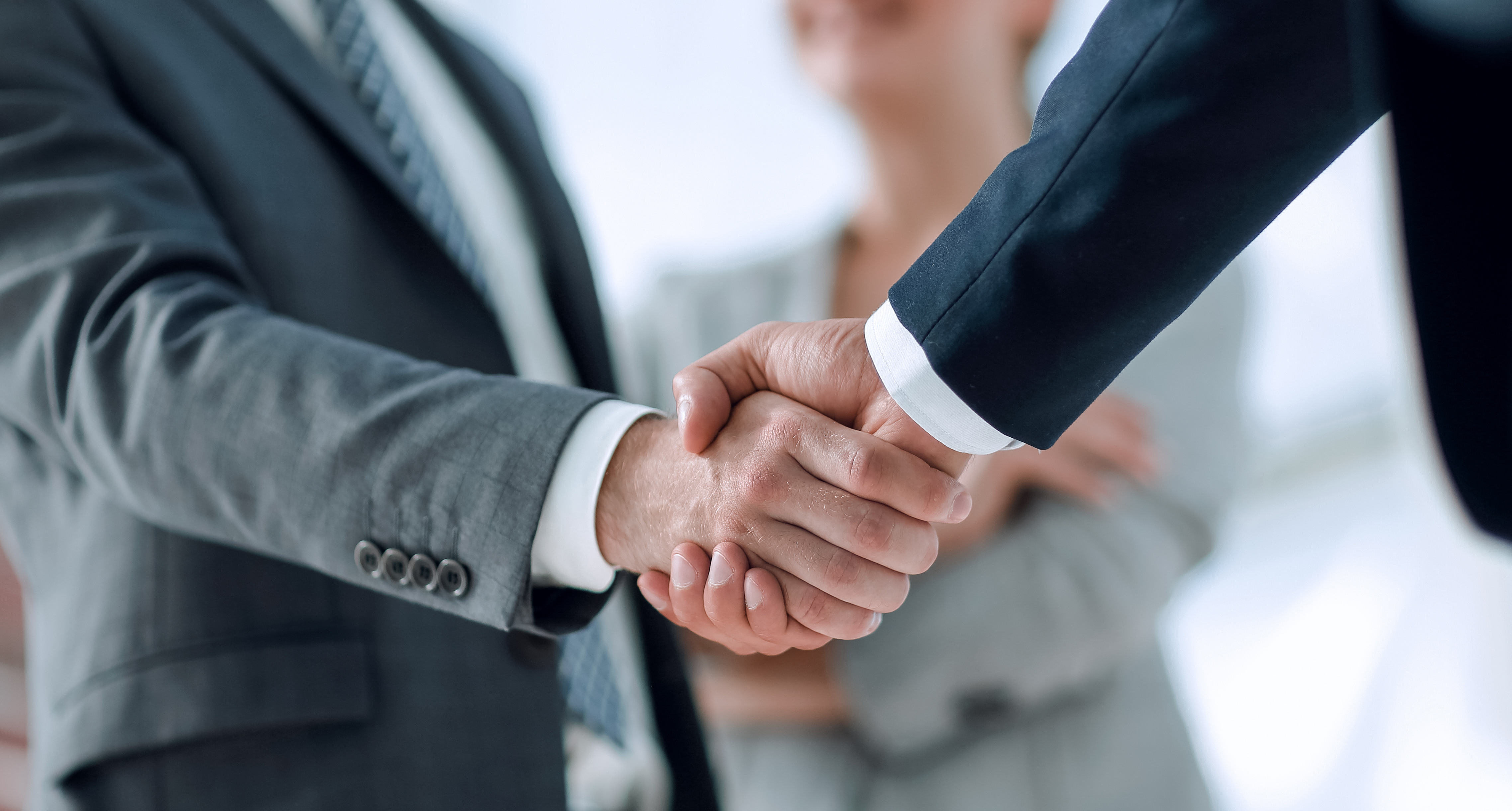 Two business professionals in suits shake hands in a formal agreement or partnership gesture.