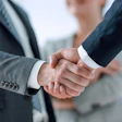 Two business professionals in suits shake hands in a formal agreement or partnership gesture.