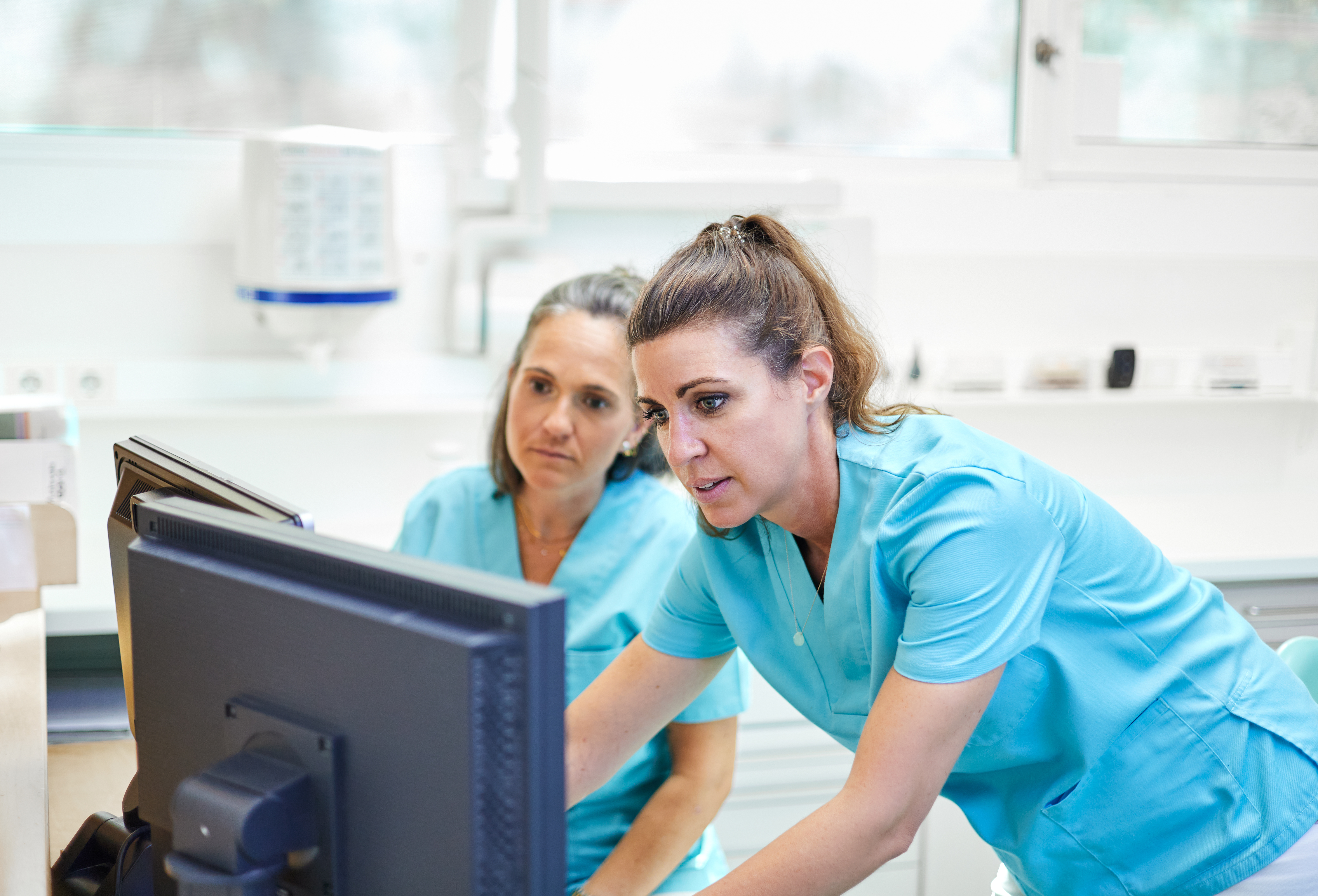 Two dental professionals look at a computer screen. They are troubleshooting a software issue.