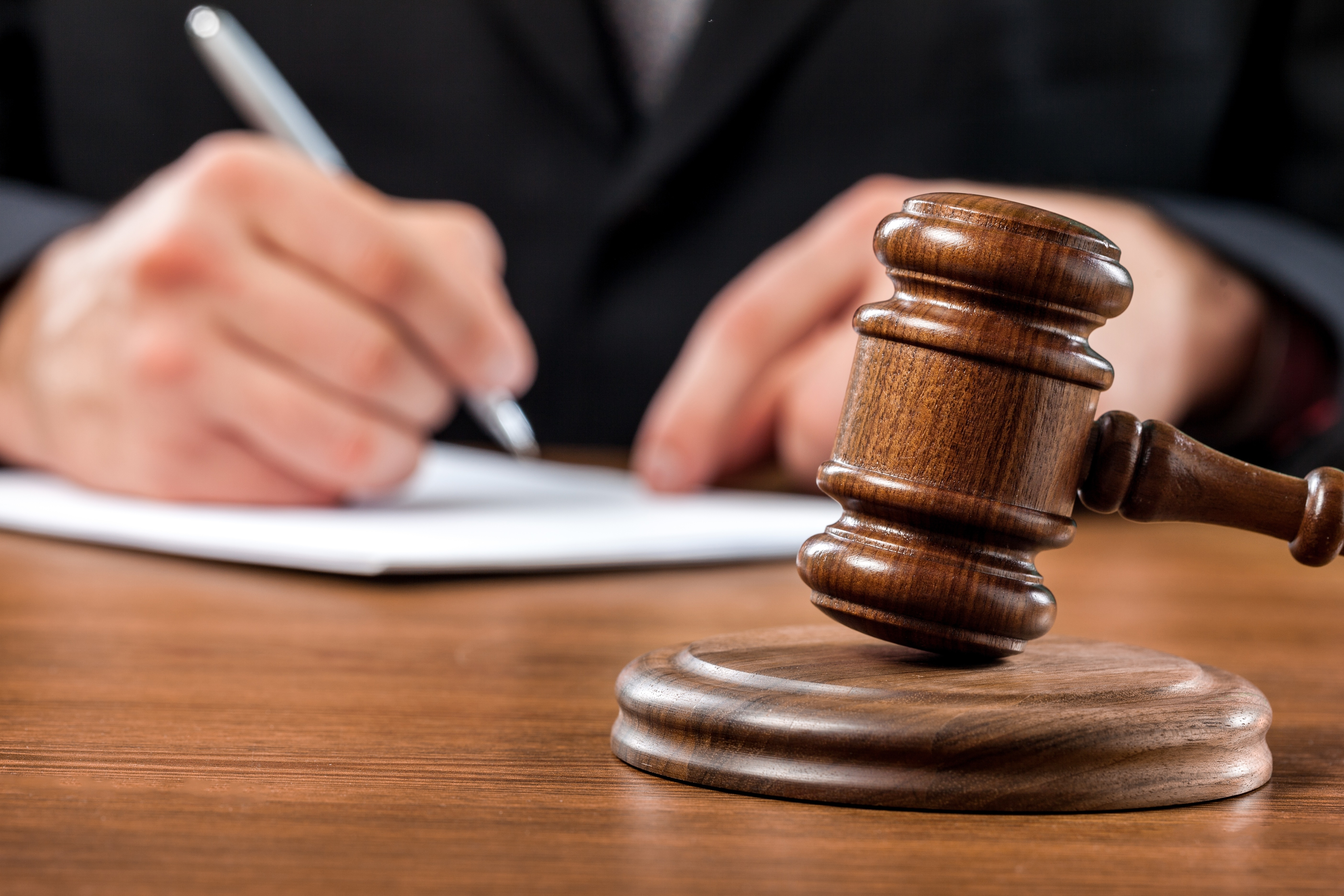 Close up of a judge's wood gavel. In the background is a judge signing a document.