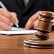 Close up of a judge's wood gavel. In the background is a judge signing a document.