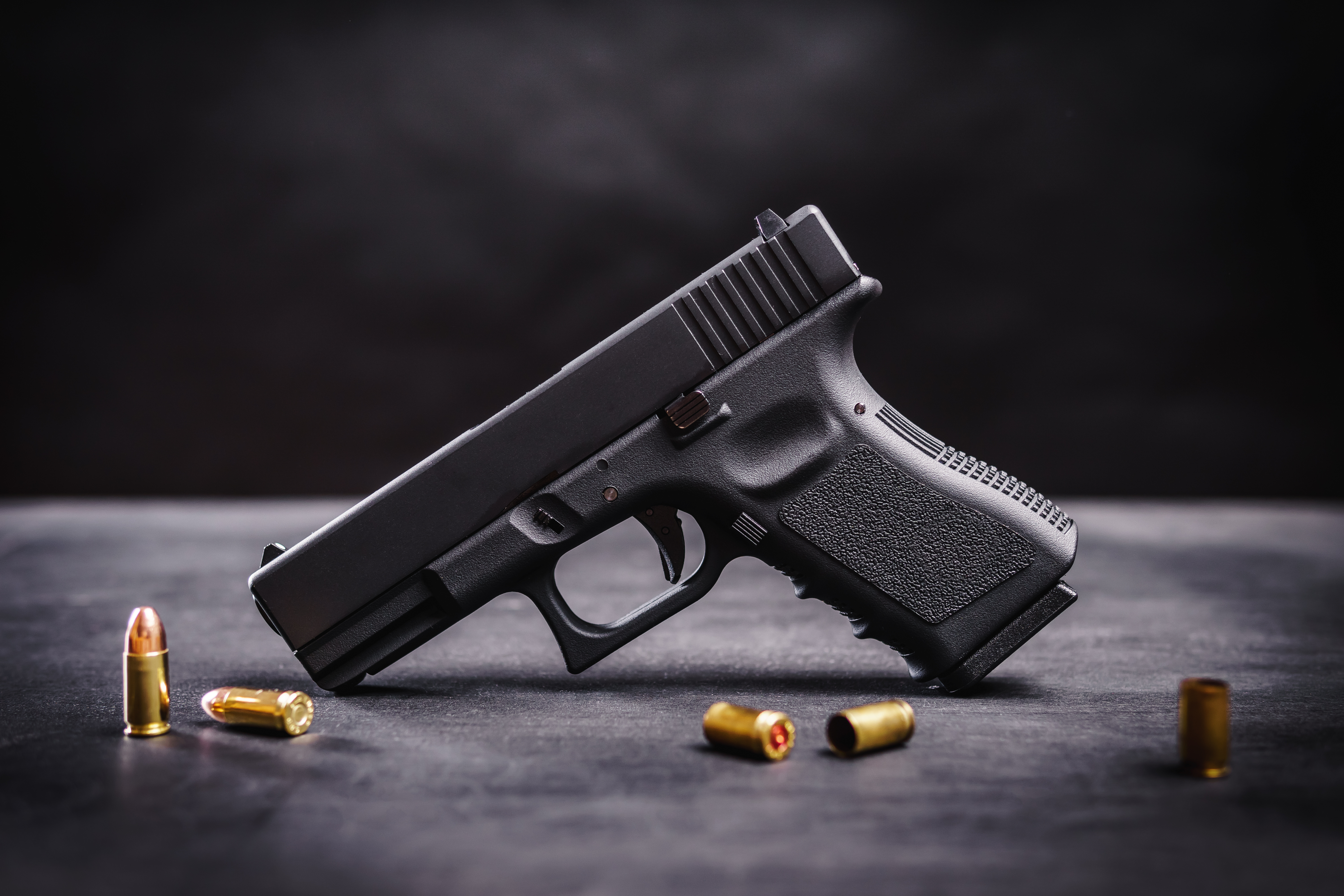 Black semi-automatic handgun with brass ammunition cartridges on a dark surface.