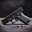 Black semi-automatic handgun with brass ammunition cartridges on a dark surface.