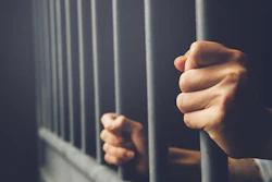 Hands grip prison bars in dim lighting, symbolizing incarceration and confinement.